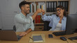 © Krakenimages.com - Man and woman celebrating a fist bump in an office with computers, notebooks, and shelves in the background