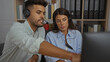 © Krakenimages.com - Man and woman working together with headsets in an office environment, focusing intently on a computer screen, indicating a collaborative business task.