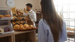 © Krakenimages.com - Woman observing as a man, possibly a baker, arranges bread in a bakery shop interior, showcasing various pastries and breads displayed on shelves and counter, under soft indoor lighting.