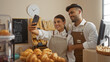 © Krakenimages.com - Man and woman taking selfie together in bakery shop with bread and pastries in the background, both wearing aprons and smiling