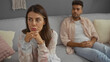 © Krakenimages.com - Woman thinking while man sitting on couch in living room, suggesting relationship issues and indoor stress