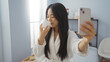 © Krakenimages.com - Asian woman taking a selfie and smelling a skincare product in a spa room, emphasizing self-care and relaxation in a calming wellness center.