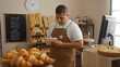 © Krakenimages.com - Young, hispanic, man working in a bakery shop, taking notes while surrounded by fresh baked bread and pastries in an indoor setting.