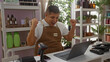 © Krakenimages.com - Young hispanic man celebrating while working on a laptop in a decorated shop with shelves of products and plants