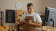 © Krakenimages.com - Young hispanic man working in bakery shop interior checking his phone while wearing a brown apron