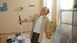 © Krakenimages.com - Woman laughing joyfully while painting a new living room, amidst home renovation with painting supplies on the floor, in a sunlit apartment interior.