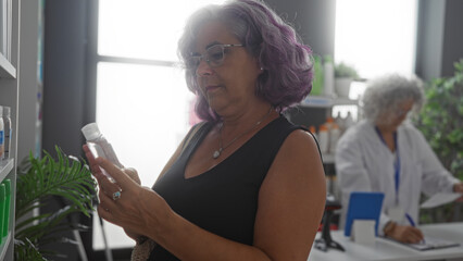 Mature woman examining a product in a pharmacy with a pharmacist working in the background