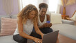 © Krakenimages.com - Women using a laptop together in a cozy living room, with one holding a credit card while the other types on the keyboard, indicating online shopping or banking activities at home