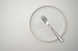 © Alina Pitiel - White plate on a white table. There is a fork on the plate. Top view, copy space