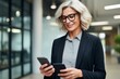 © juliars - Smiling businesswoman comparing information on two smartphones while walking through a modern office hallway