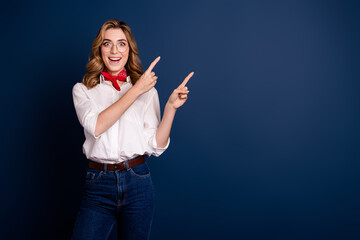 Wall Mural - Fashionable young woman in white shirt and scarf excitedly pointing on dark blue background