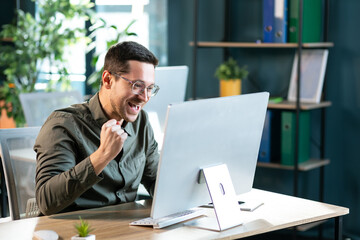 Excited worker sitting at desk in coworking space use computer reading message looking at device screen received great unbelievable opportunity or reward. Motivated employee celebrating job promotion