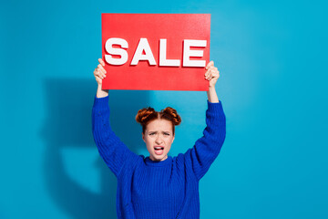 Wall Mural - Young woman in a blue sweater holding a red sale sign on a blue background