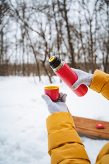 Wall Mural - A person is holding a thermos and a cup in the snow