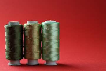 Spools of colorful sewing threads on red background, space for text