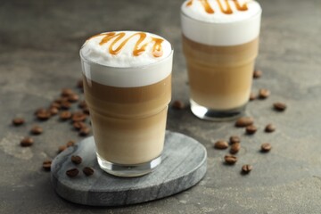 Wall Mural - Tasty latte macchiato in glasses and coffee beans on grey table, closeup