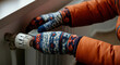 © Alexandr - Freezing person adjusting a radiator valve while wearing cozy knitted gloves