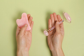 Wall Mural - Woman with face roller and gua sha tool on light green background, top view