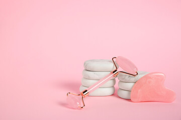 Wall Mural - Face roller, gua sha tool and massage stones on pink background. Space for text