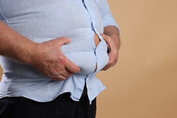 Wall Mural - Overweight man in tight shirt on beige background, closeup. Space for text