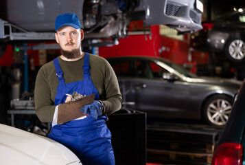 Wall Mural - Portrait of professional auto mechanic in uniform with paper holder in a car service center