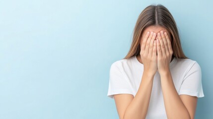 Wall Mural - Young Woman Hiding Face with Hands, Expressing Feelings of Sadness or Anxiety Against Light Blue Background