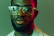 © SHOTPRIME STUDIO - Portrait of a young African man wearing trendy glasses with an expressive gaze, set against a vibrant green and pink background, emphasizing modern fashion