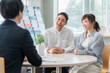 © buritora - ショールーム・商談スペースで話を聞く夫婦と接客するビジネスマン