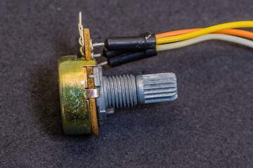 A metal potentiometer with wires attached, lying on a dark background