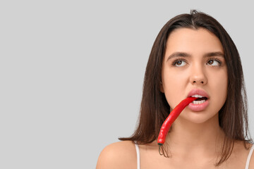 Poster - Beautiful young woman with red chili pepper in her mouth on grey background