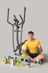 Wall Mural - Young man with bottles of water and sports equipment on grey background