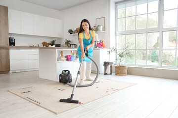 Wall Mural - Young woman vacuuming carpet  in kitchen