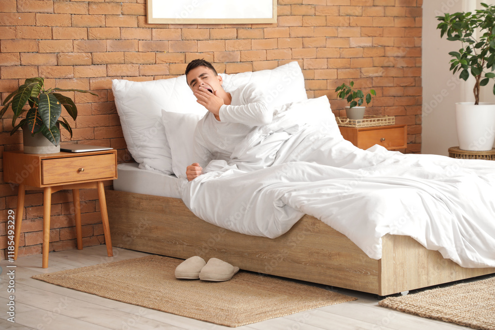 Young man yawning in cozy bed at home
