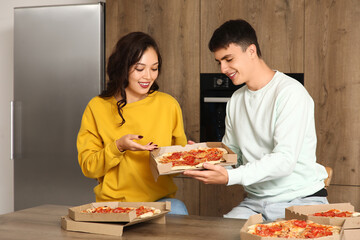 Wall Mural - Young couple eating pepperoni pizza at table in kitchen