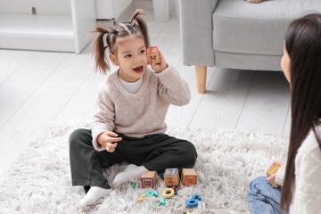 Wall Mural - Cute little girl with cube and teacher learning alphabet on carpet at home