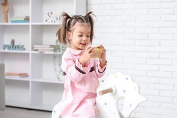 Wall Mural - Cute little girl holding cubes with letters on rocking horse at home