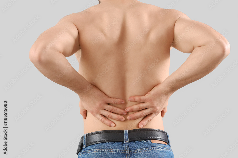 Young man with naked torso suffering from back pain on light background, closeup