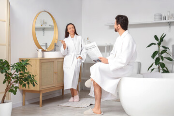 Wall Mural - Beautiful woman brushing teeth while her husband reading newspaper in bathroom