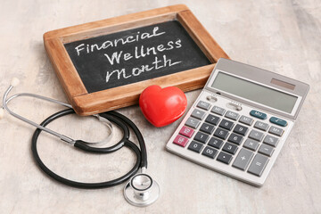 Wall Mural - Stethoscope, red heart, calculator and chalkboard with text FINANCIAL WELLNESS MONTH on grunge background