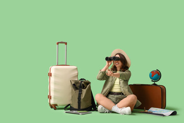 Wall Mural - Female traveler with bags looking through binoculars on green background. Itinerary concept