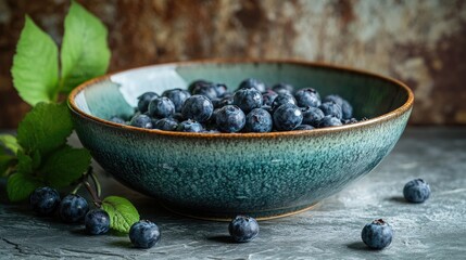 Canvas Print - Freshly picked ripe blueberries arranged in a rustic ceramic bowl with green leaves on a textured background.