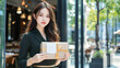 © S.JR Stocker - A young Asian female entrepreneur stands outside her upscale restaurant, proudly holding a neatly wrapped package with a blank label for mock-up purposes.