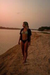Wall Mural - young brazilian woman in swimwear walking along a serene beach at sunset