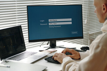 Programmer sitting at table in office and entering password on computer