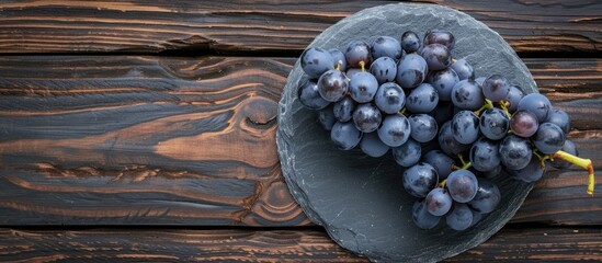 Aufkleber - Bunch of Blue Isabella grapes and a round stone slate plate on a wooden background Copyspace for text Flat lay