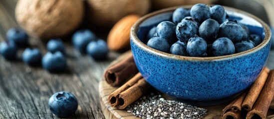 Fototapete - Healthy natural food concept A close up of fresh blueberries in a blue bowl with blurry granola and chia seeds featured in a shallow depth of field On a wooden board there are some almonds cinnamon