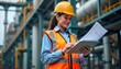 © miss irine - Female engineer in safety vest, helmet examines blueprints, tablet. Surveys oil refinery plant site. Focus on meticulous inspection, tech use at industrial workplace. Working on production process.