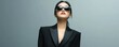 © Viacheslav - Asian woman in black suit and sunglasses on grey background, exuding confidence and elegance with a poised stance, perfect for themes of fashion, professionalism, and chic