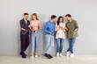 © Studio Romantic - Young people with smartphones. Group of men and women standing in office and using mobile phones. Several friends leaning on wall, holding cellphones, sharing files, discussing news, showing photos