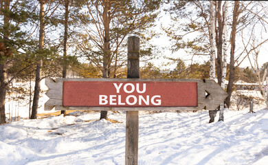 Wall Mural - Belonging and you belong symbol. Concept words You belong on beautiful wooden old retro vintage road sign. Beautiful winter forest background. Business belonging and you belong concept. Copy space.